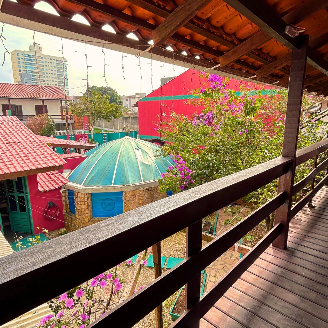 Varanda de madeira com vista para o jardim e os telhados da pousada