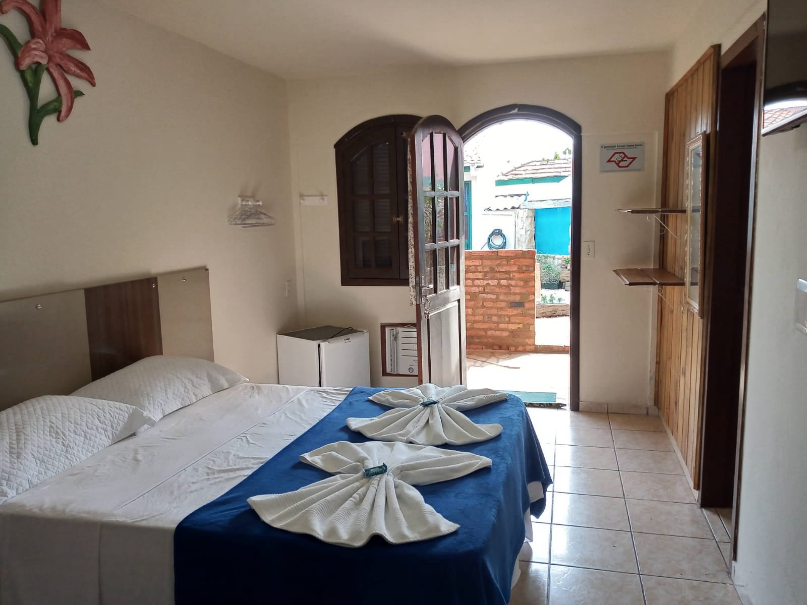 Quarto de casal da pousada com porta em arco, cama preparada e frigobar